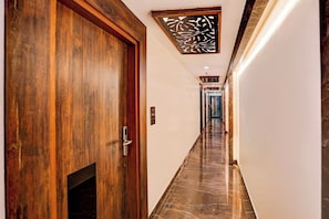 A hallway with a wooden door, a fire alarm, and a marble floor.