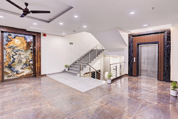 A hotel lobby with a marble floor, a staircase, a ceiling fan, and a large decorative wall.