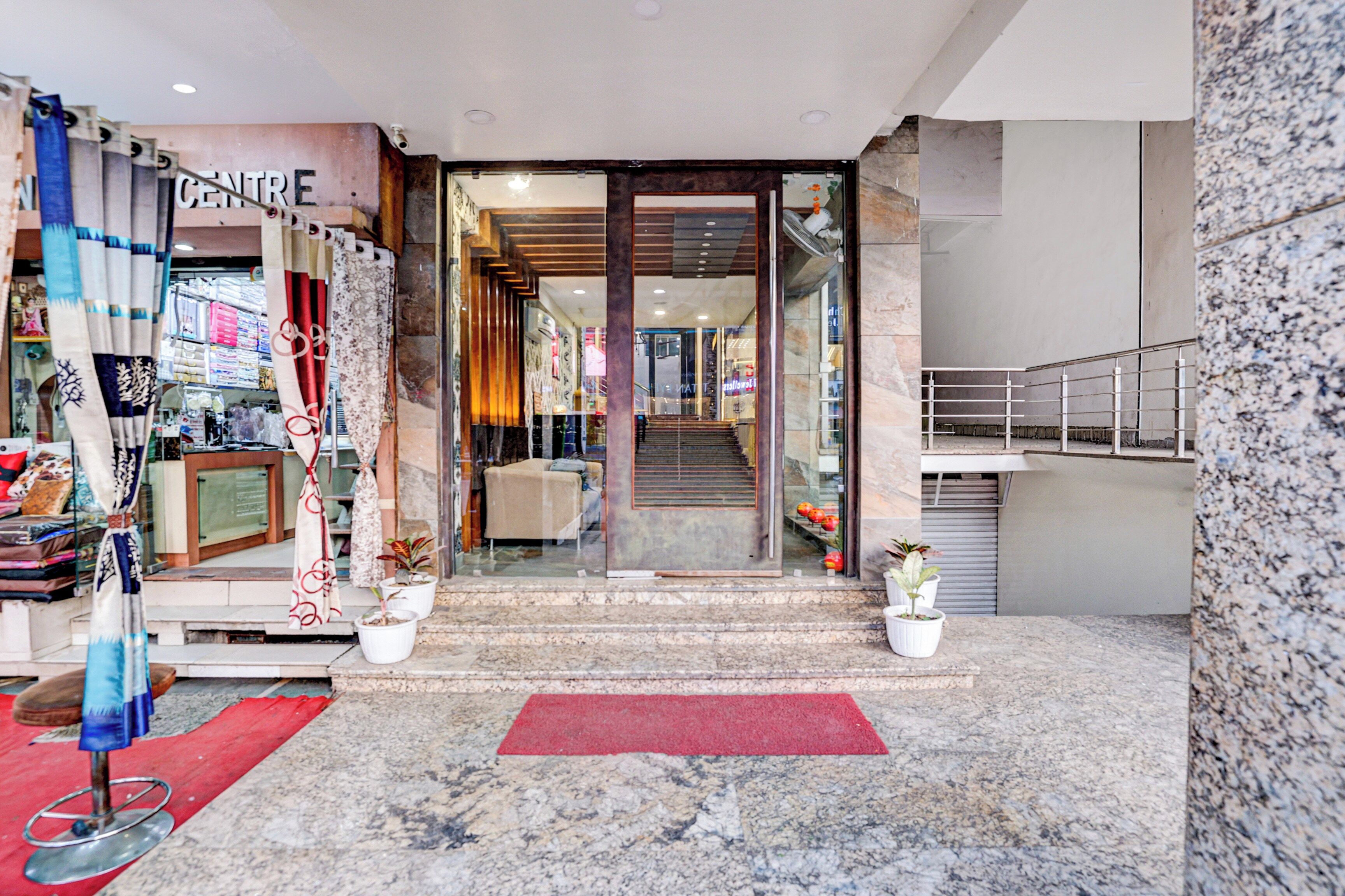 Entrada de hotel con mostrador de recepción, una escalera que conduce al piso superior y una alfombra roja.