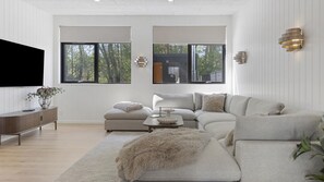 A modern living room with a sectional sofa, a flat-screen TV, and a large window offering a view of trees. - VillaVilla 1011 - Fjellerup, Østjylland (Glesborg)