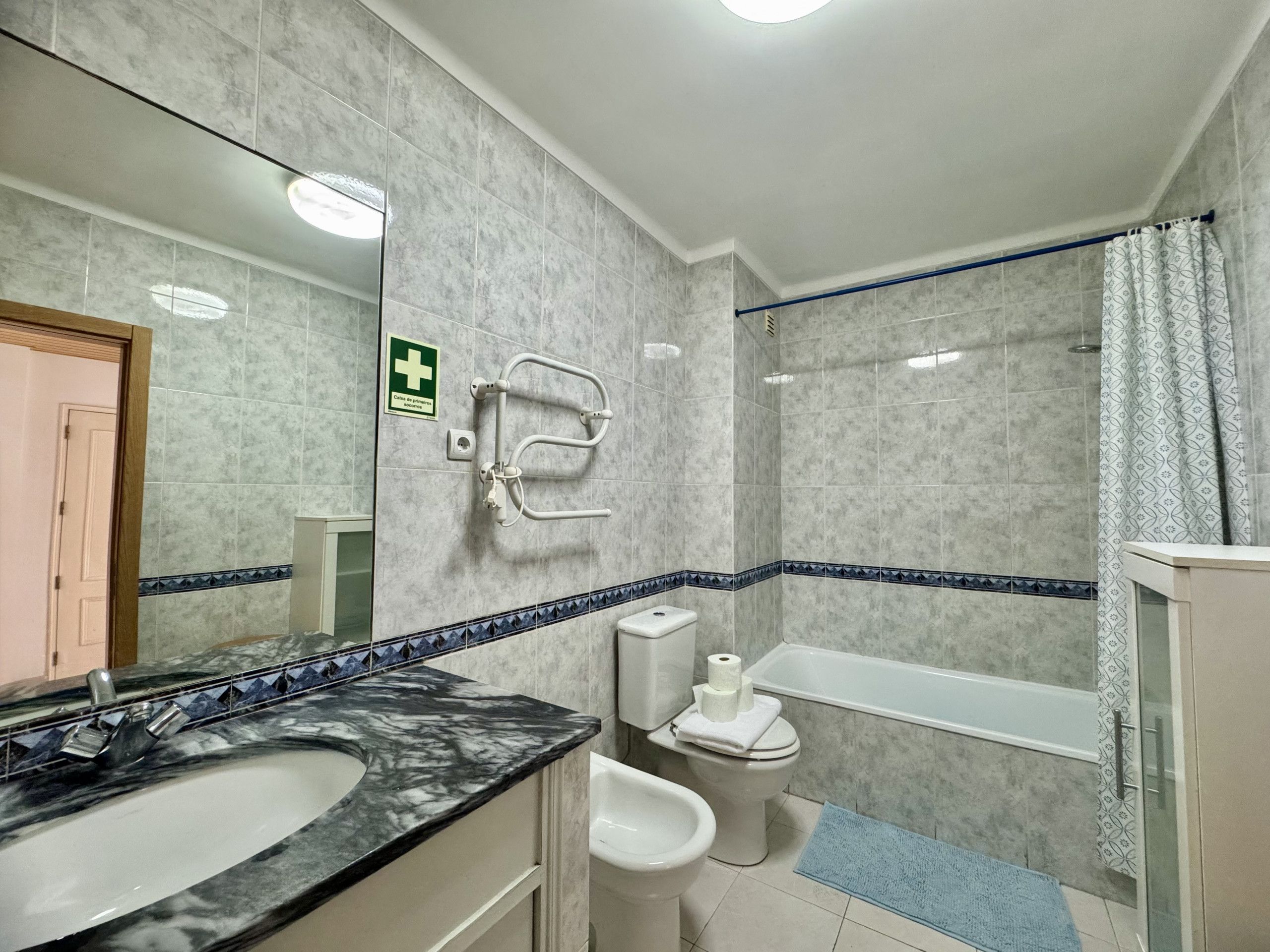 A bathroom with a marble sink, a toilet, a bidet, a shower with a curtain, and a handrail.