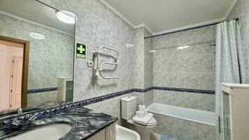A bathroom with a marble sink, a toilet, a bidet, a shower with a curtain, and a handrail.