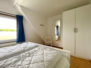 Ein Schlafzimmer mit einem Bett, einem Schrank, einem Spiegel und einem Fenster mit Vorhängen.