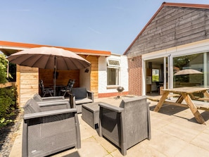 Eine Terrassenanlage im Freien mit Korbmöbeln, einem Grill und einem Holztisch.