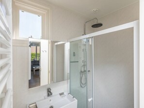 Ein modernes Badezimmer mit einer Duschkabine, einem weißen Waschbecken und einem großen Spiegel.
