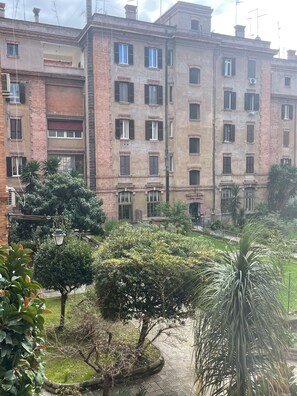 Un edificio residencial de varios pisos con balcones, un jardín con diversas plantas y un camino pavimentado.