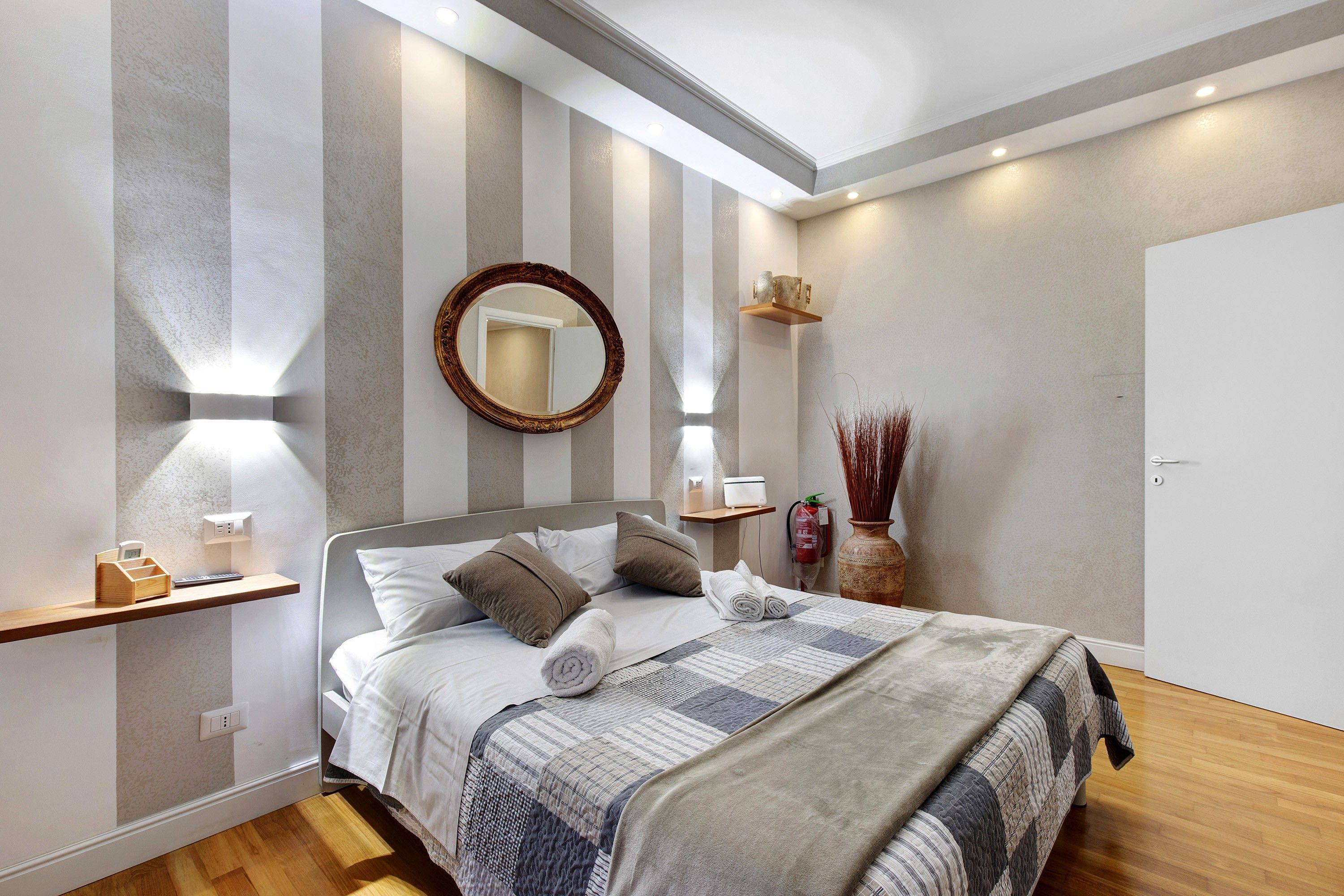 A modern bedroom with a bed, bedside tables, a mirror, and a vase.