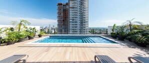 Ein Poolbereich auf dem Dach mit Blick auf ein Hochhaus, umgeben von Blumentöpfen.
