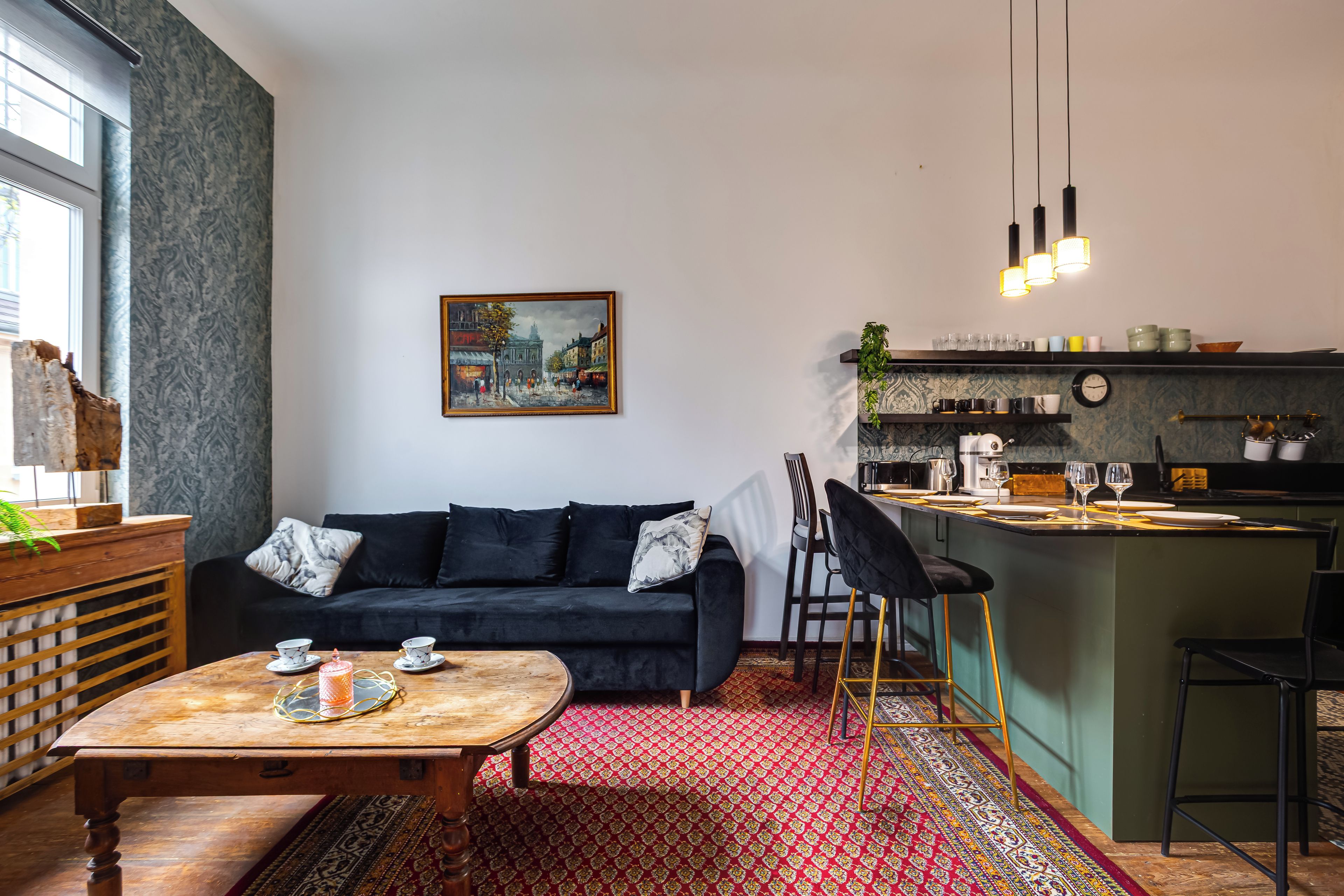 A modern living room with a dark sofa, a wooden coffee table, and a red patterned rug.