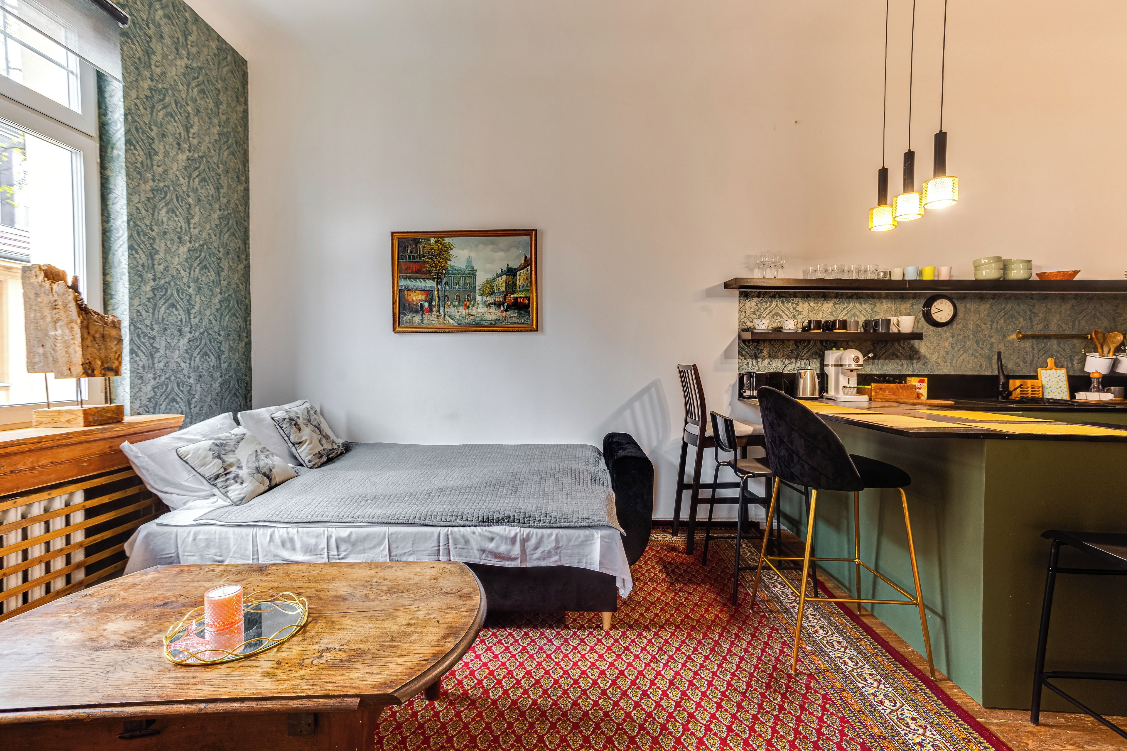 A compact room with a bed, a dining table, a kitchen area, and a painting on the wall.