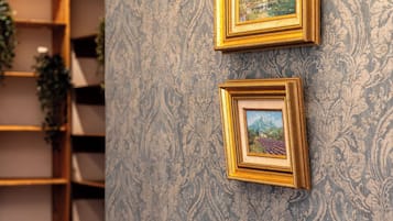 Una habitación con dos cuadros en la pared, un banco de madera con plantas en macetas y un papel tapiz estampado.