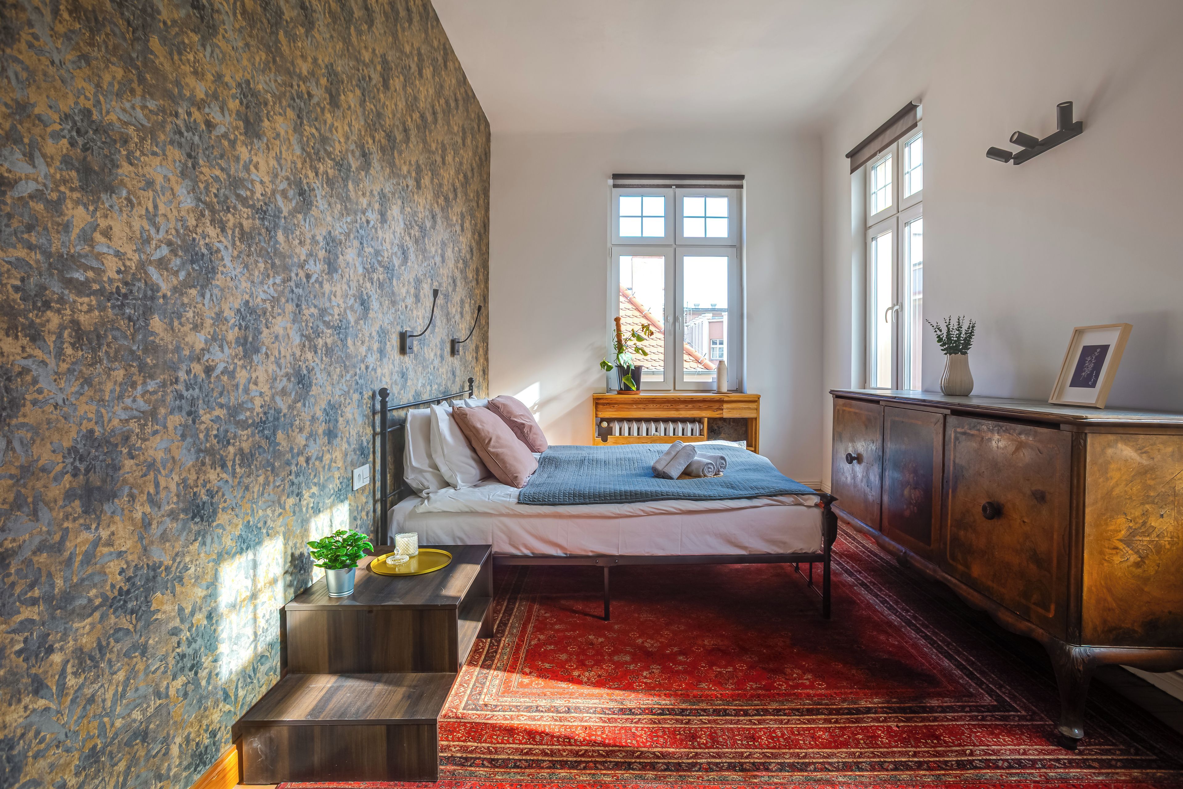 A bedroom with a bed, a nightstand, a dresser, a window, and a patterned wall.