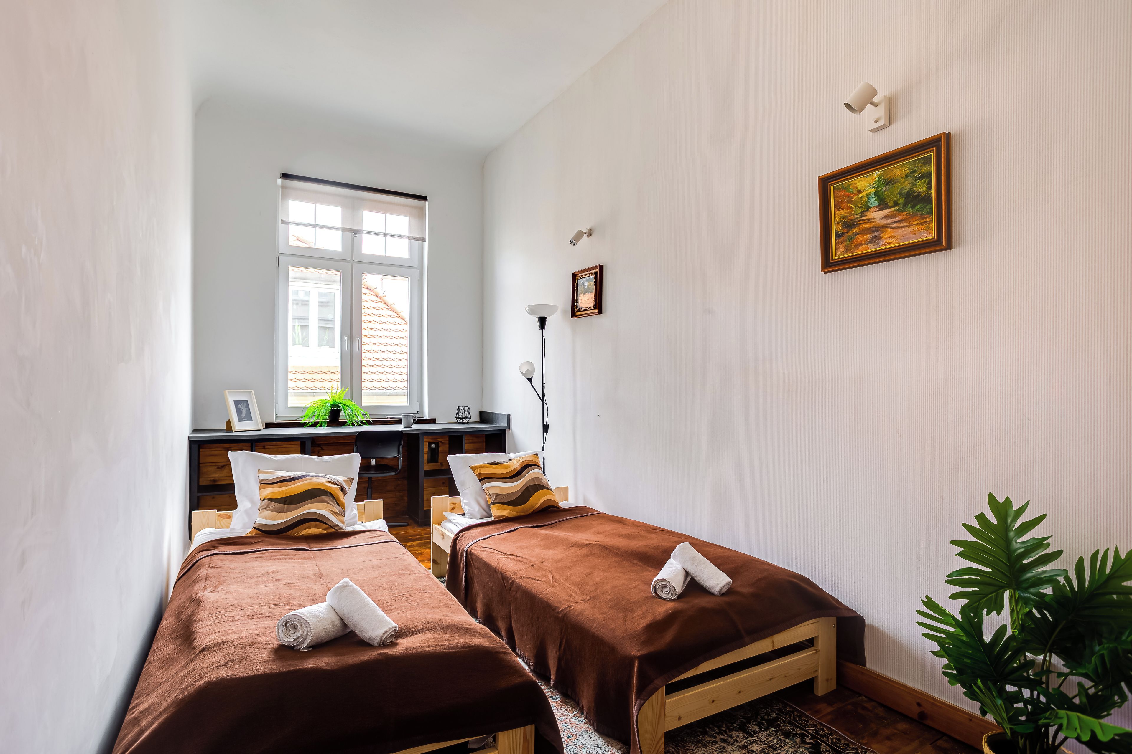 Una habitación con dos camas, un escritorio, una silla, un ventanal y una planta.