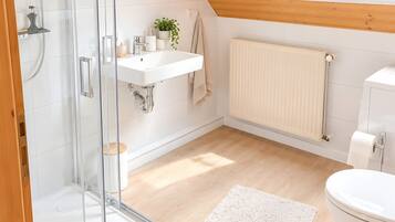 Ein modernes Badezimmer mit Duschkabine aus Glas, einem Waschbecken, einer Toilette und einem Fenster mit Blick auf Grünflächen.
