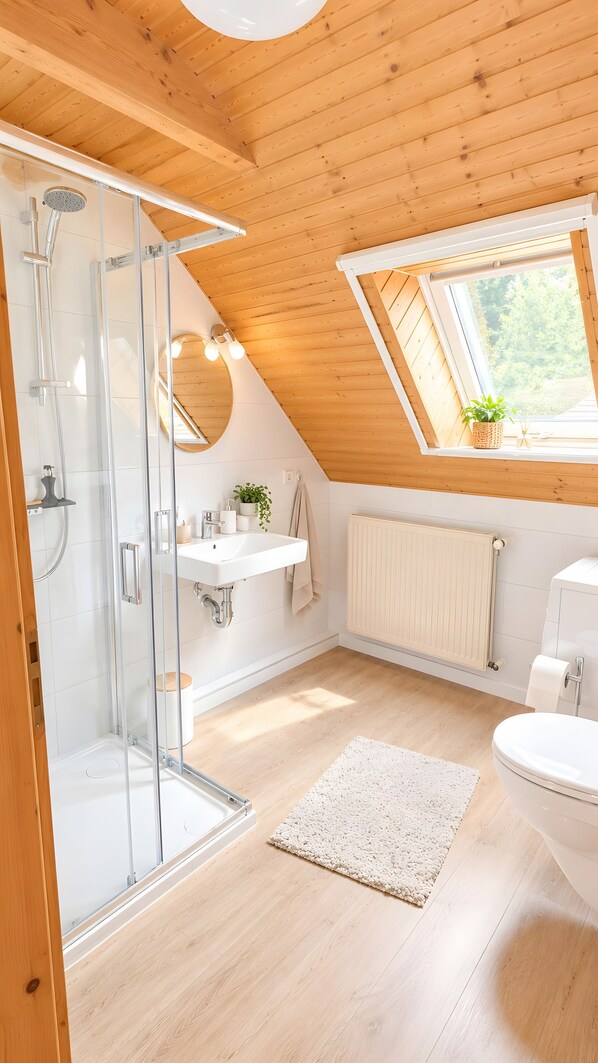 A modern bathroom with a glass shower enclosure, a sink, a toilet, and a window with a view of greenery.