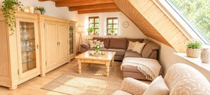 Ein gemütliches Schlafzimmer im Loft-Stil mit schrägem Dach, einem Holzschrank, einer Couch, einem Tisch und einem Fenster mit Blick auf Grünflächen.