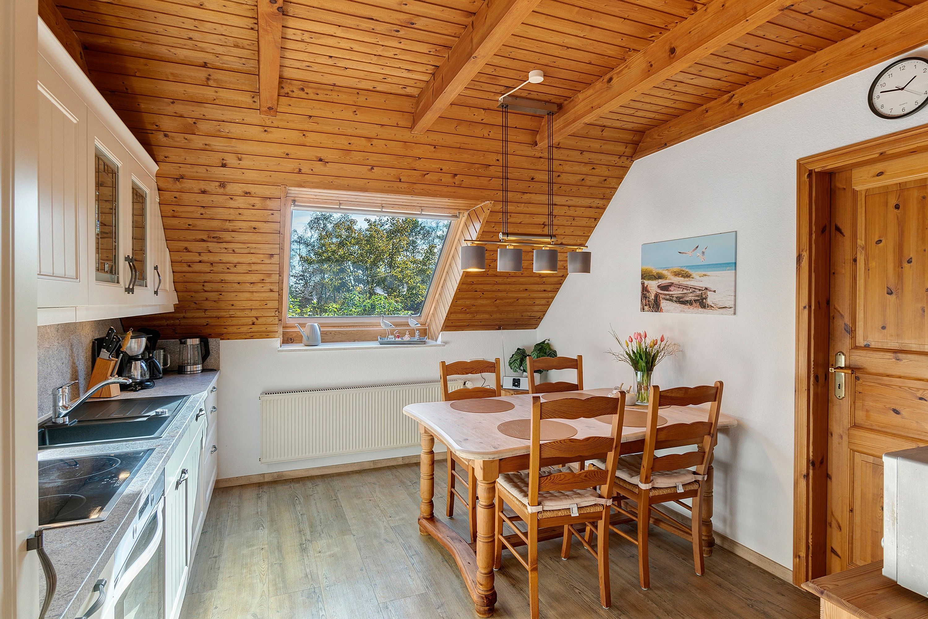 Eine gemütliche Küche mit Essbereich, Holzbalken an der Decke, einem Fenster mit Aussicht und einer Uhr an der Wand.