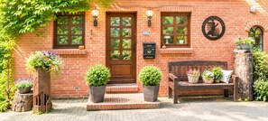 A brick building with a wooden bench, potted plants, and a mailbox.