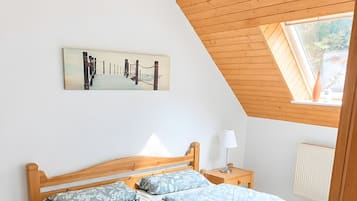 Ein Schlafzimmer mit Holzboden, einem Bett mit gemusterten Bettbezügen, einem Nachttisch, einer Lampe und einem Gemälde an der Wand.