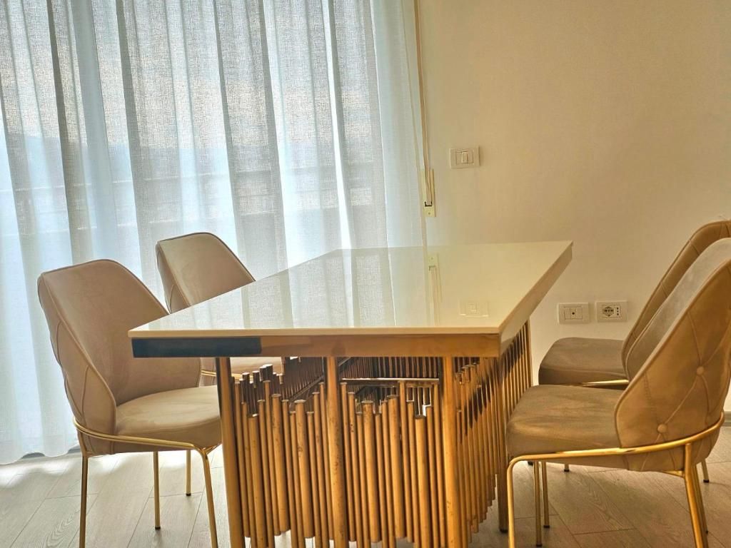 Un comedor moderno con una mesa de vidrio y cuatro sillas tapizadas con patas doradas.