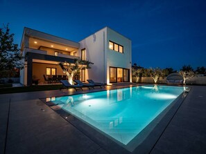 Ein modernes, zweistöckiges Haus mit Swimmingpool, Außenmöbeln und einer gut beleuchteten Terrasse.