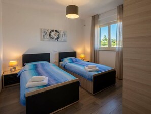 Ein Hotelzimmer mit zwei Betten, einer Deckenleuchte, einem Fenster mit Vorhängen und einem Wandbild.