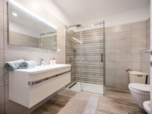 Ein modernes Badezimmer mit einer Duschkabine aus Glas, einem weißen Waschtisch mit Spiegel und einer Toilette.