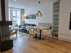 A modern living room with a dining area, a fireplace, and a large window. - Captain's House Thule - Sea Buckthorn (Langeoog)