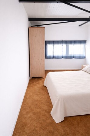 A bedroom with a bed, a window with curtains, a wardrobe, and a brown carpet.