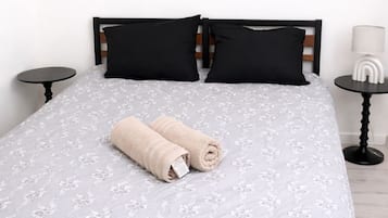 Un lit avec une couvre-lit à motifs floraux, deux oreillers noirs et deux serviettes enroulées.
