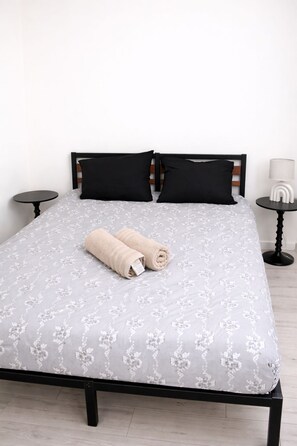A bed with a floral-patterned bedspread, two black pillows, and two rolled towels.