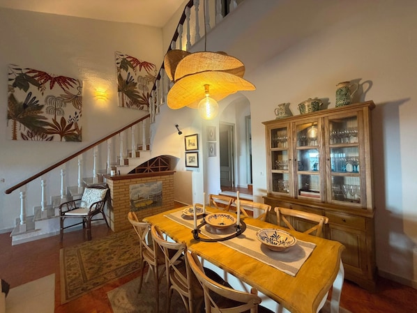 A dining area with a wooden table, chairs, a chandelier, and a staircase with a railing.