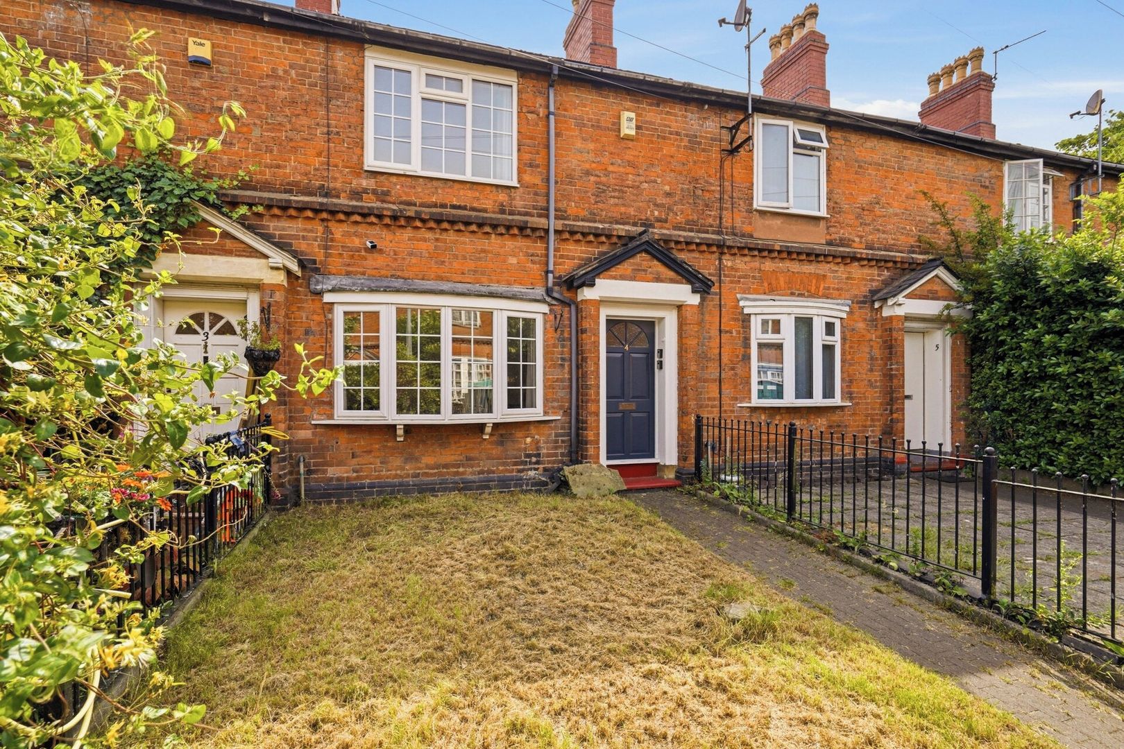 A two-story brick house with a front garden, a black metal fence, and a clear sky.