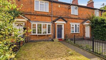 A two-story brick house with a front garden, a black metal fence, and a clear sky.