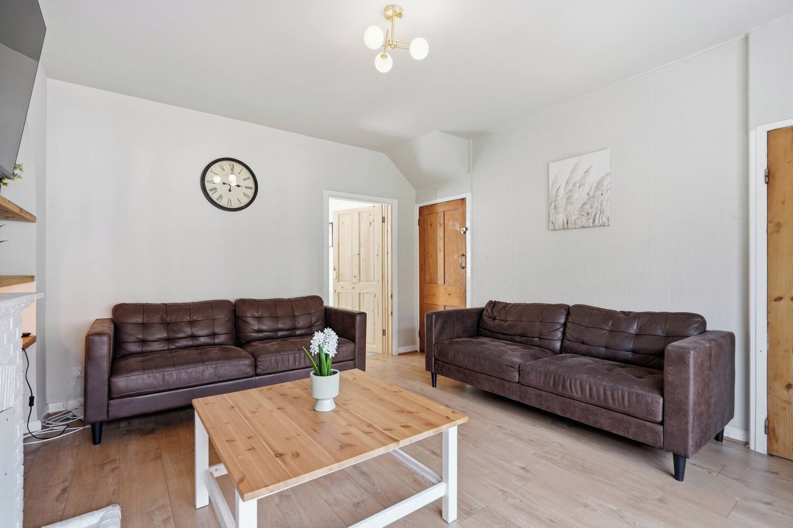 A spacious living room with two brown leather sofas, a wooden coffee table, and a wall clock.
