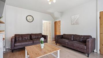 A spacious living room with two brown leather sofas, a wooden coffee table, and a wall clock.