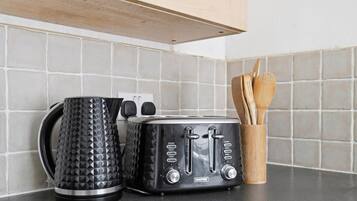 A kitchen counter with a black toaster, a black kettle, and a wooden utensil holder.