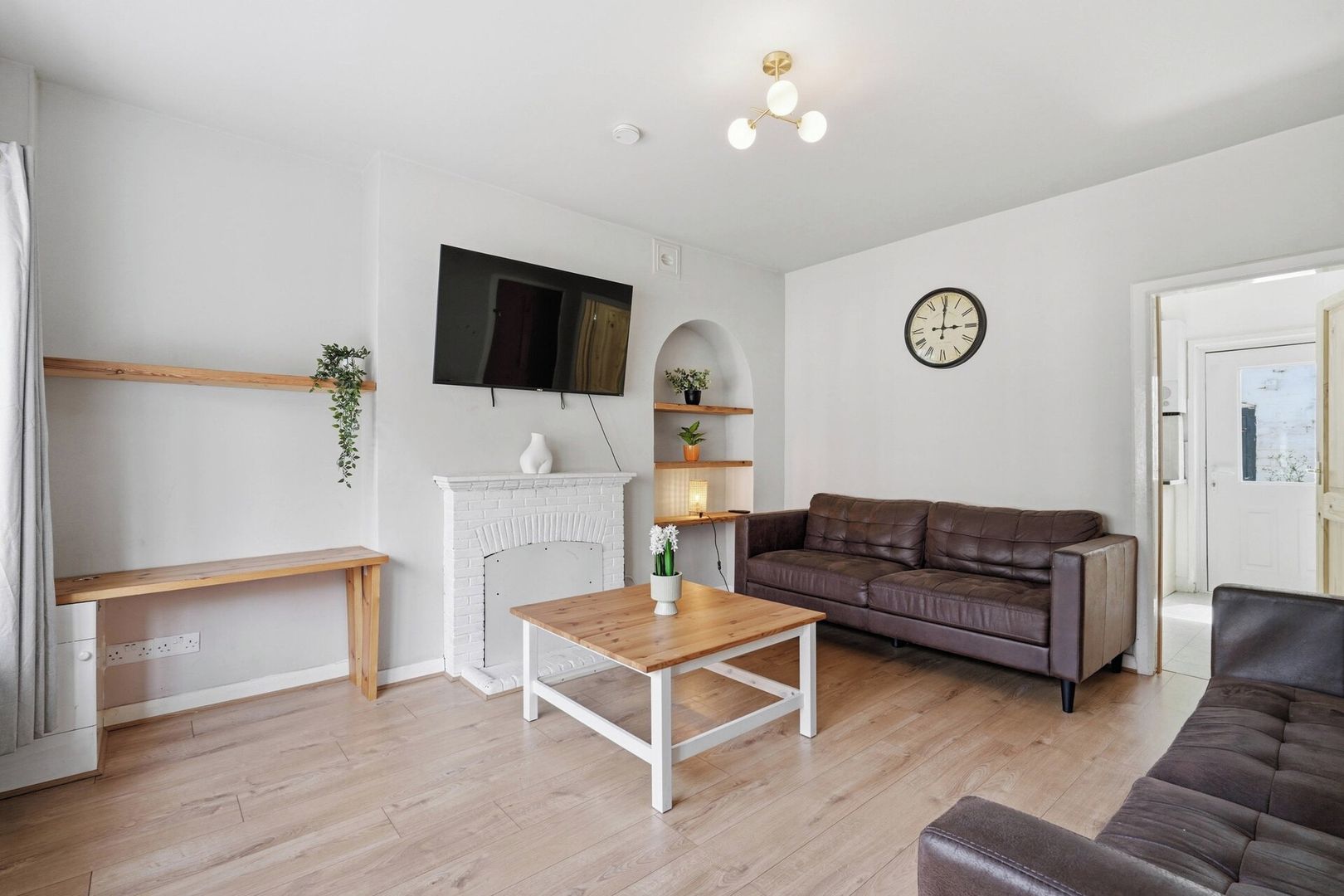A living room with a fireplace, a sofa, a coffee table, a TV mounted on the wall, and a clock.