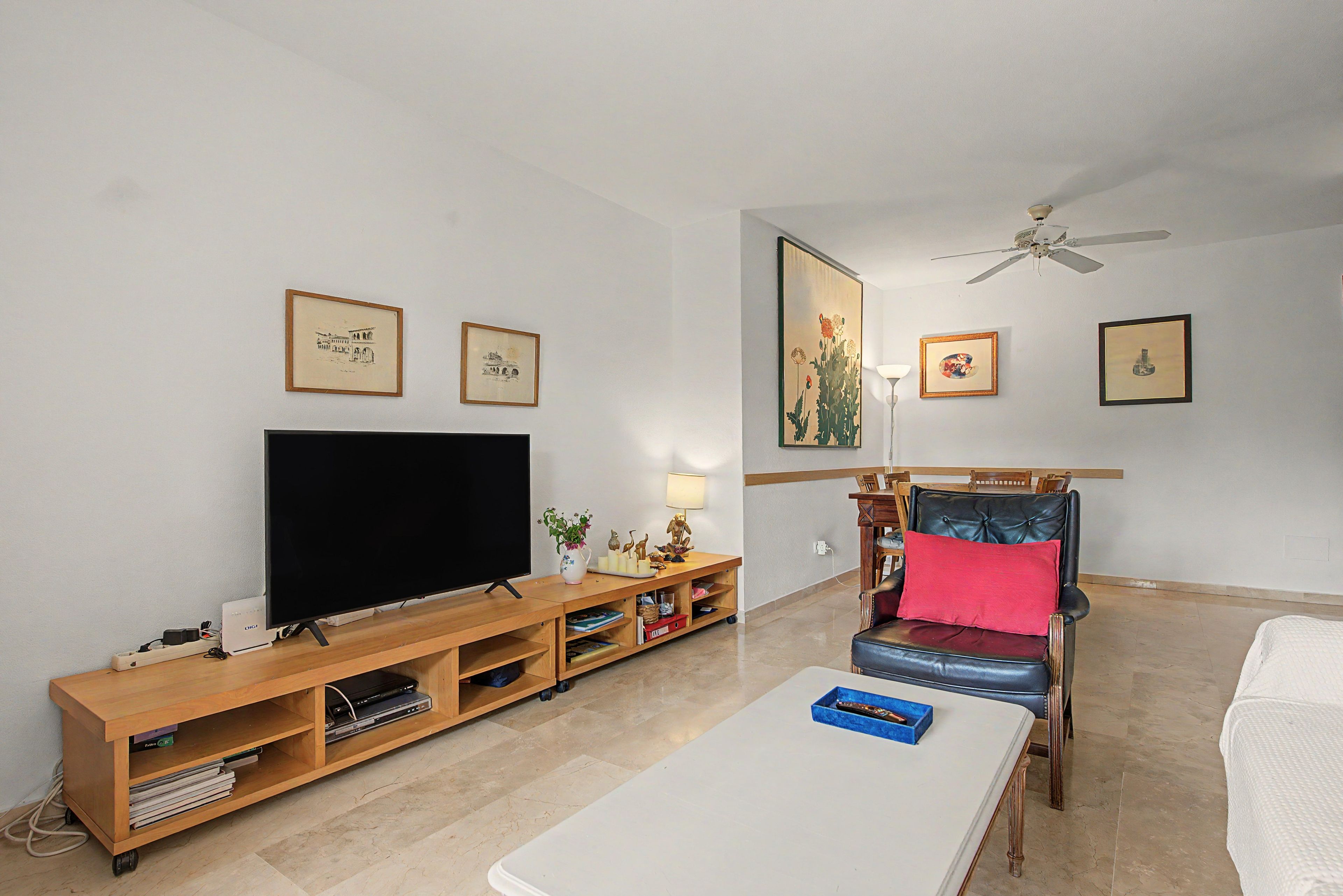 Ein Wohnzimmer mit Flachbildfernseher, einer Holzunterhaltungsecke, einem rot gepolsterten Sessel, einem weißen Couchtisch und einem Deckenventilator.