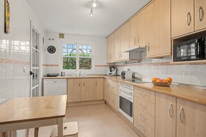 A kitchen with wooden cabinets, a microwave, a sink, and a window with a view of greenery. - Apartment 'Baviera Golf Resort' with Shared Pool, Private Terrace and Wi-Fi (Caleta de Vélez)