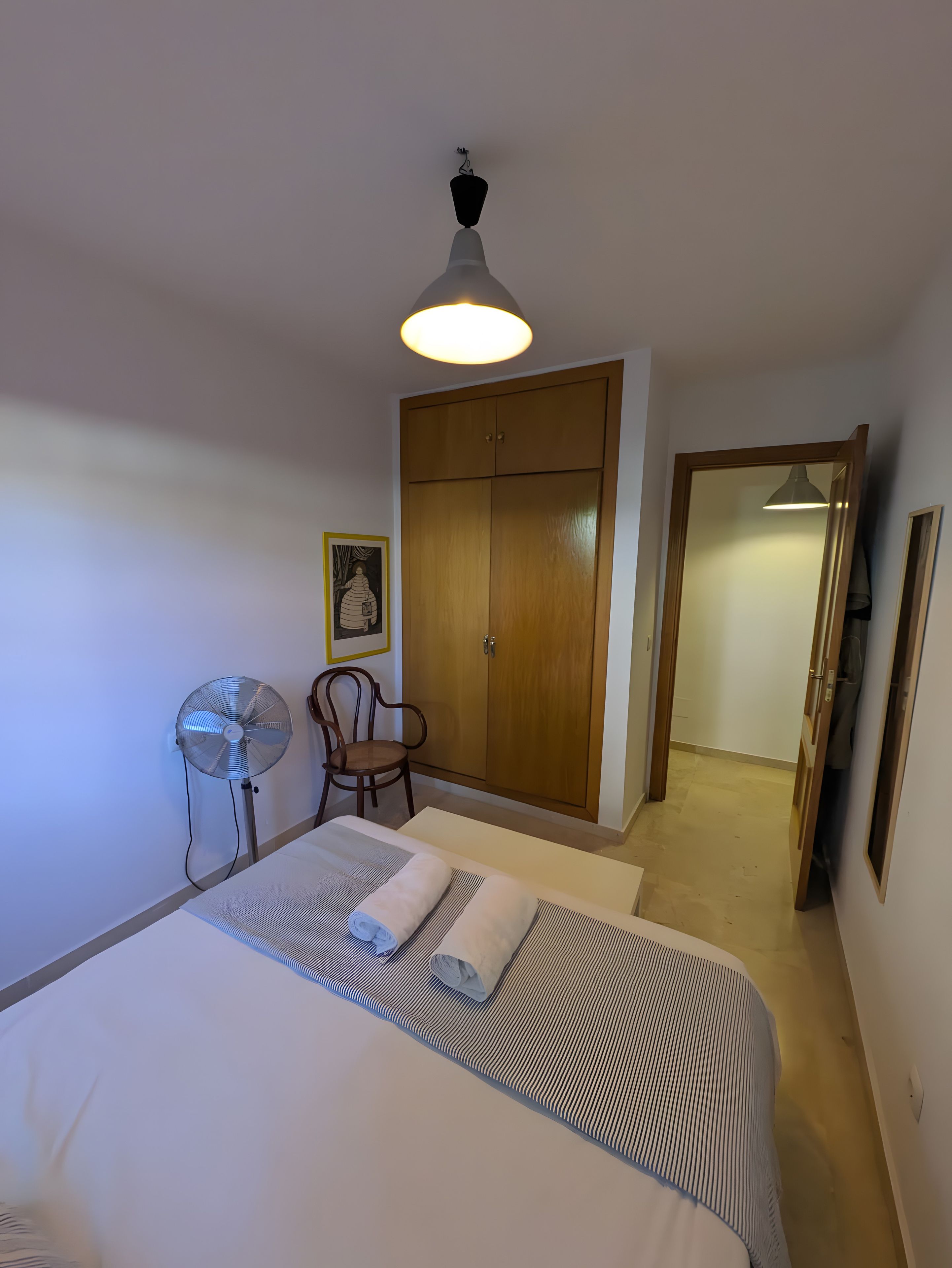 Ein Hotelzimmer mit einem Bett, einem Sessel, einem Kleiderschrank und einem Ventilator.