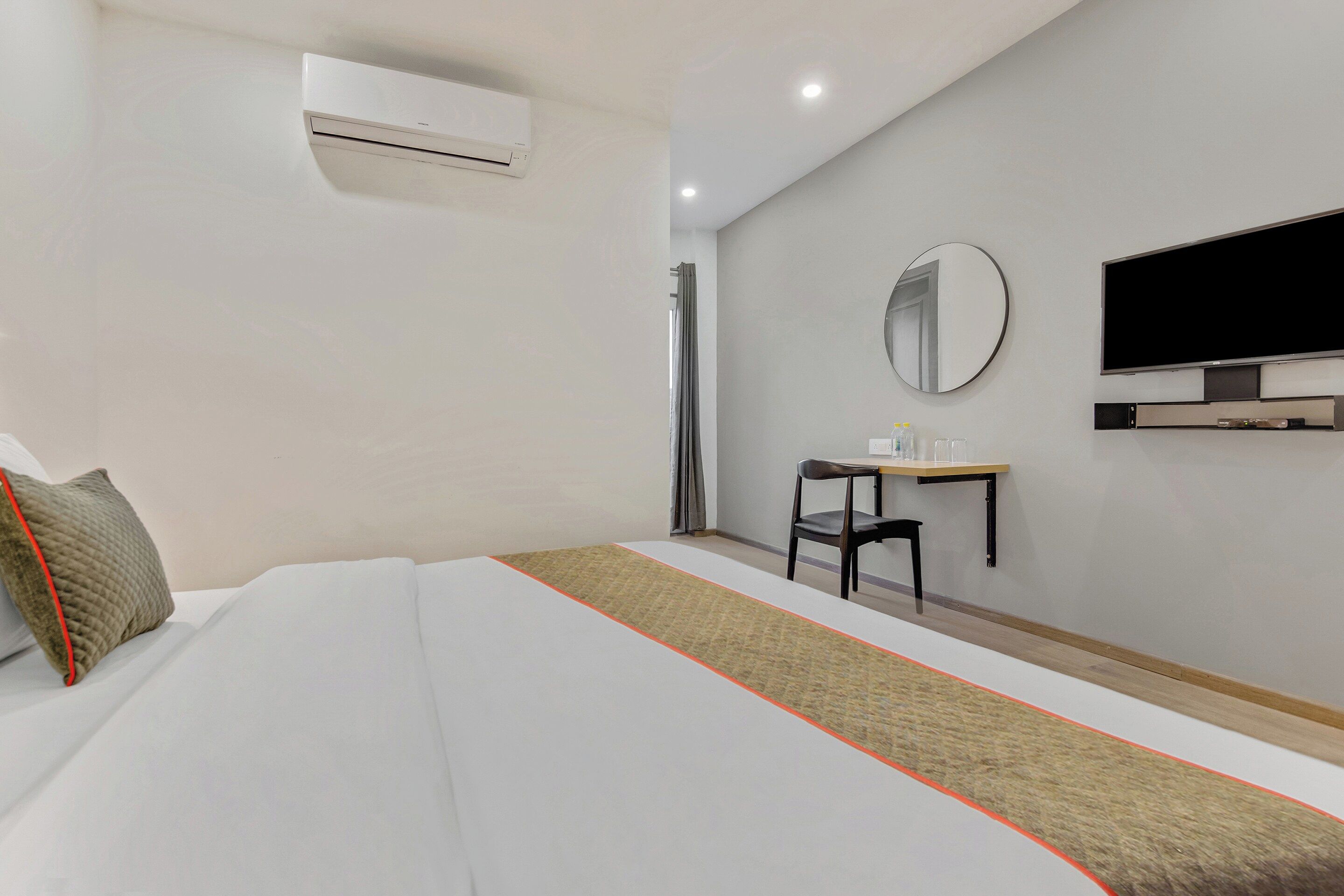 A hotel room with a bed, a desk, a chair, a television, and an air conditioning unit.