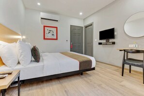 Una habitación de hotel con una cama, un escritorio, un televisor y una puerta.