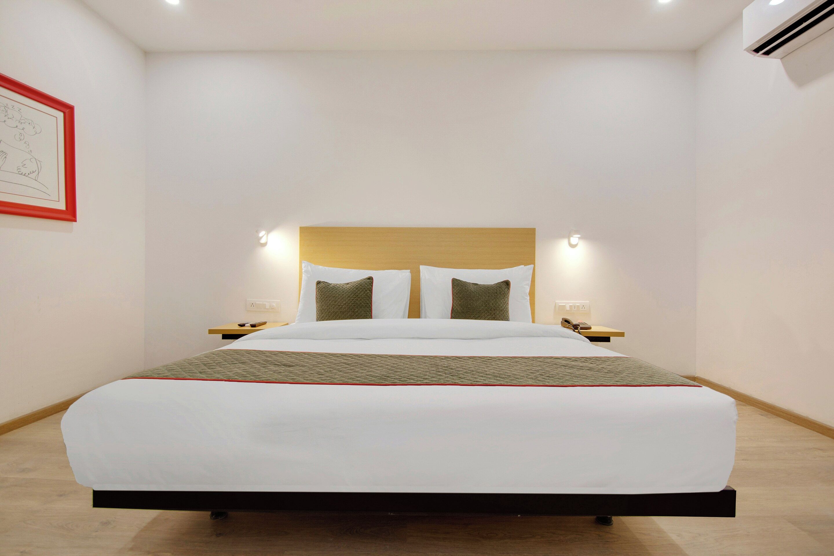 Une chambre d’hôtel avec un grand lit, deux tables de chevet, une tête de lit dotée d’un éclairage intégré et un tableau encadré au mur.