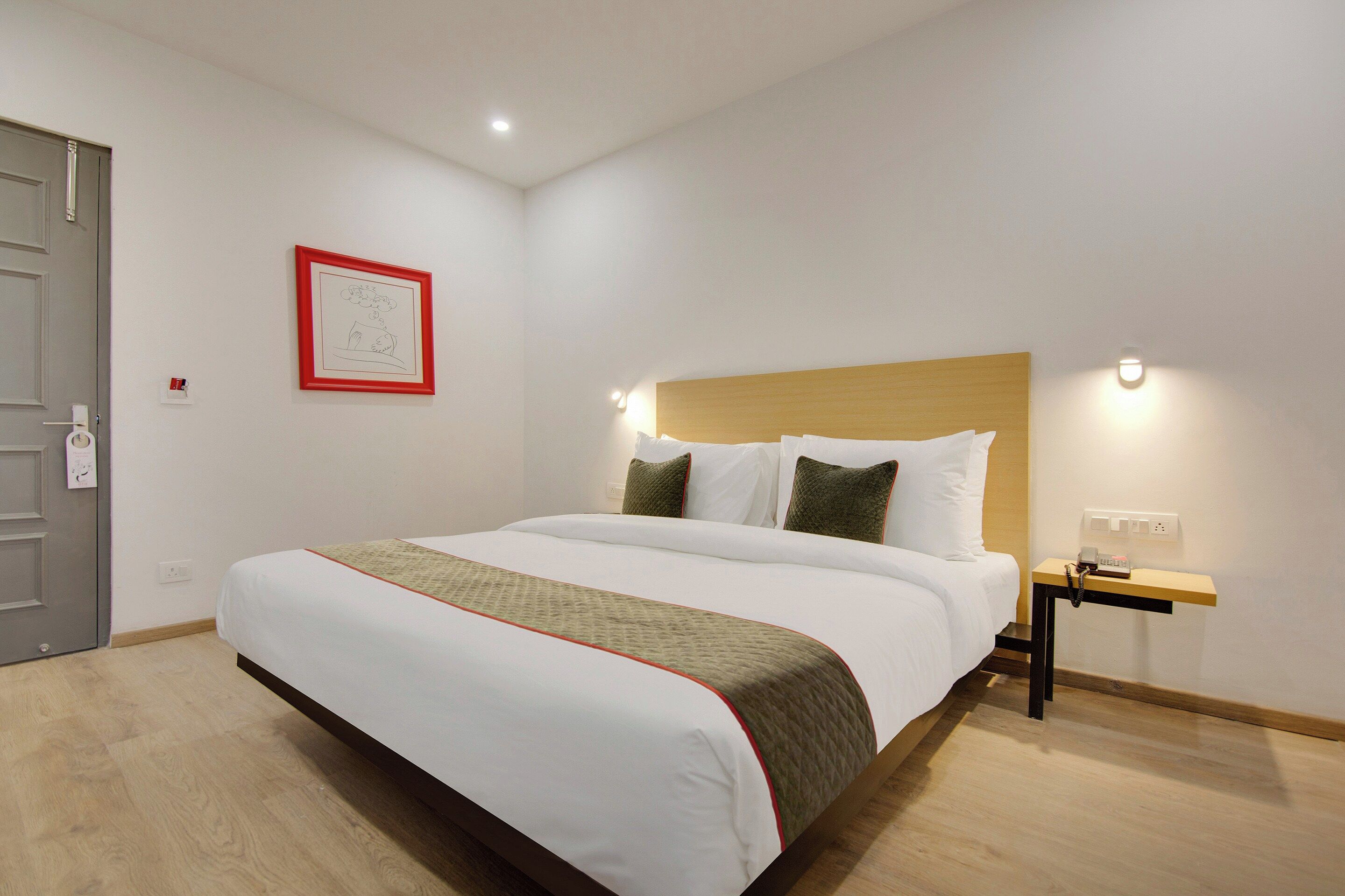 Une chambre d’hôtel avec un grand lit, une table de chevet avec un téléphone et une lampe fixée au mur.