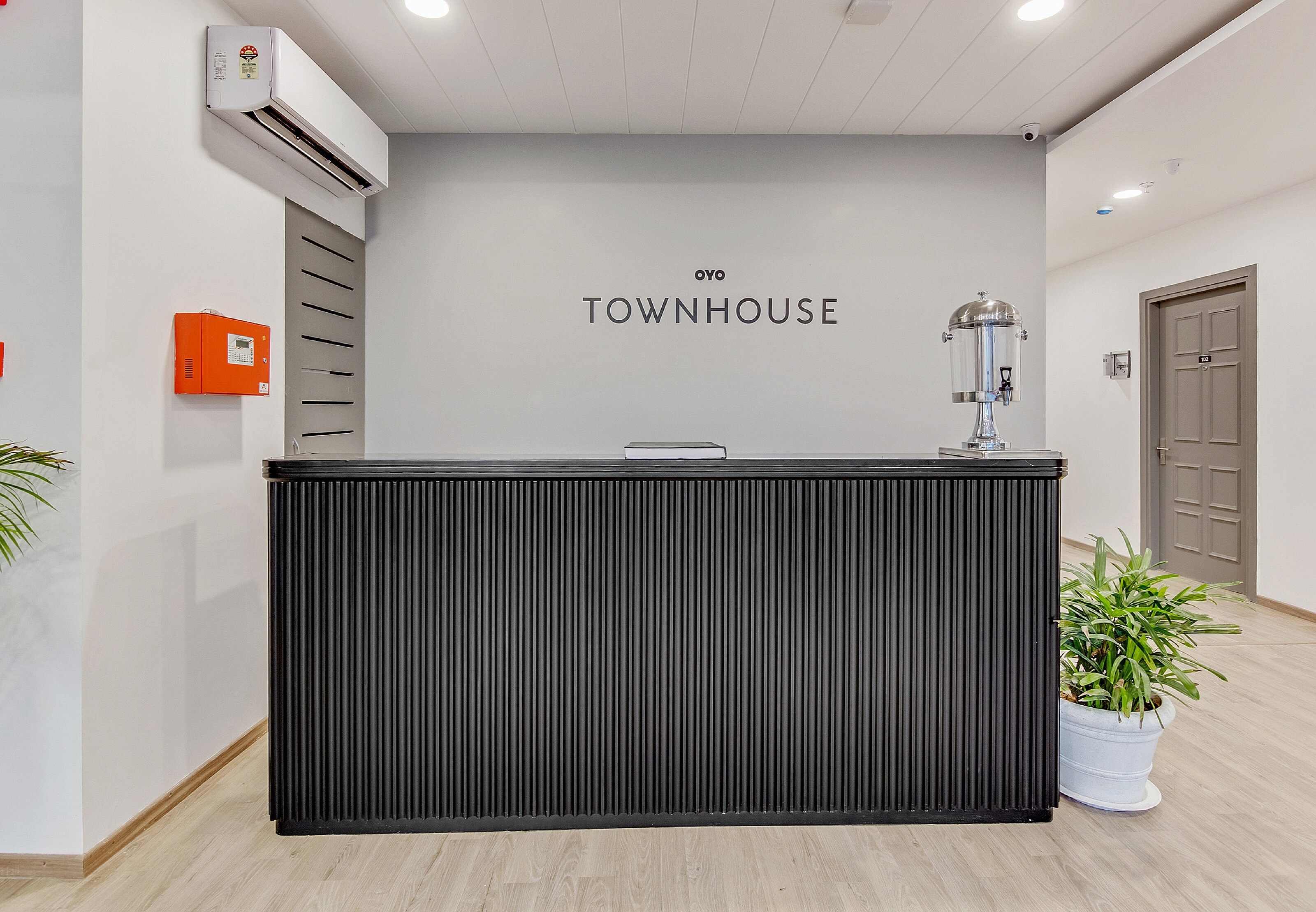 Un comptoir d’accueil avec une enseigne « TOWNHOUSE » au-dessus, un distributeur d’eau et une plante en pot sur la droite.