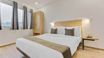Habitación de hotel con una cama grande, cabecero de madera, mesita de noche con teléfono y ventana con cortinas.