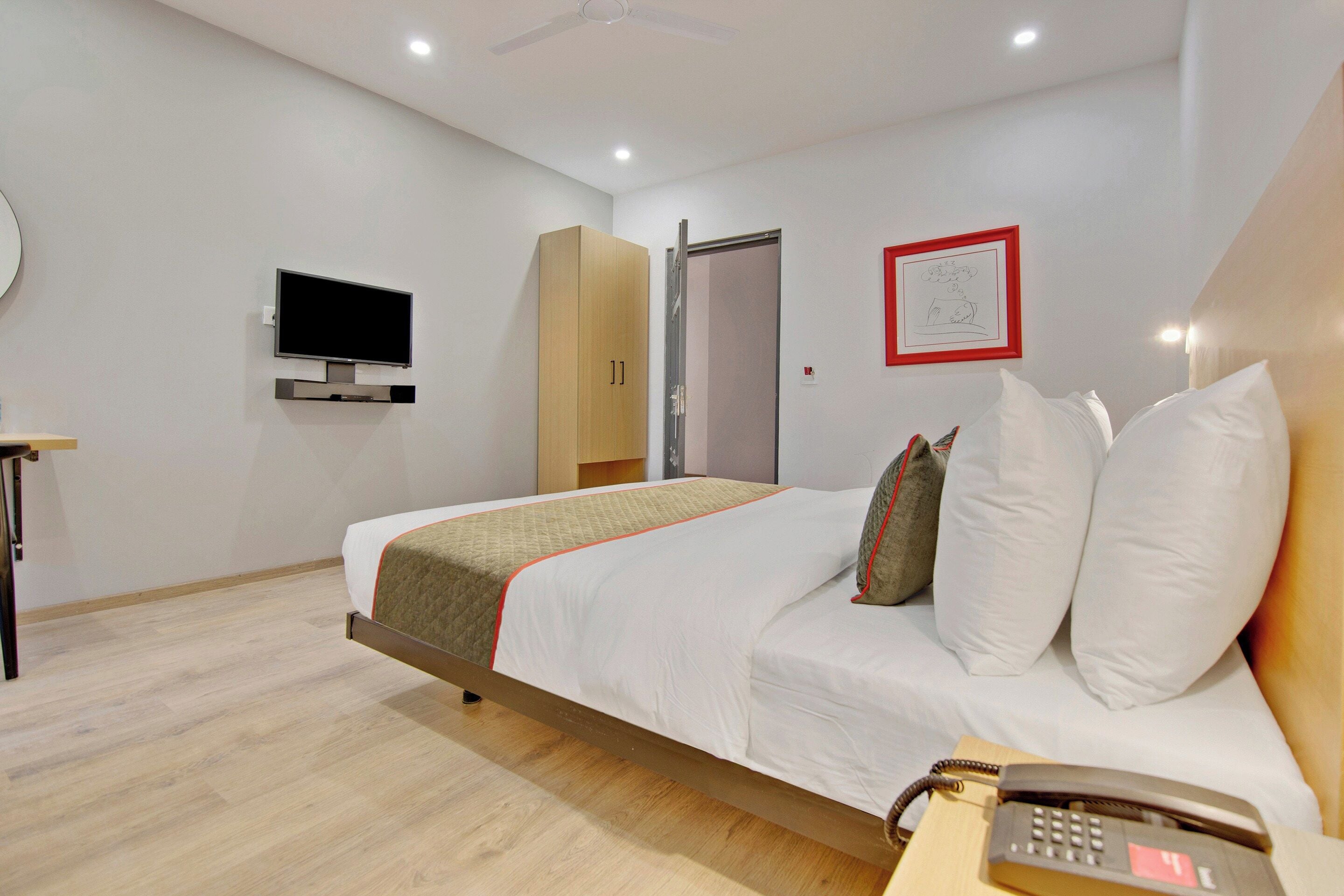 Habitación de hotel con cama, televisión, armario, puerta y un cuadro en la pared.