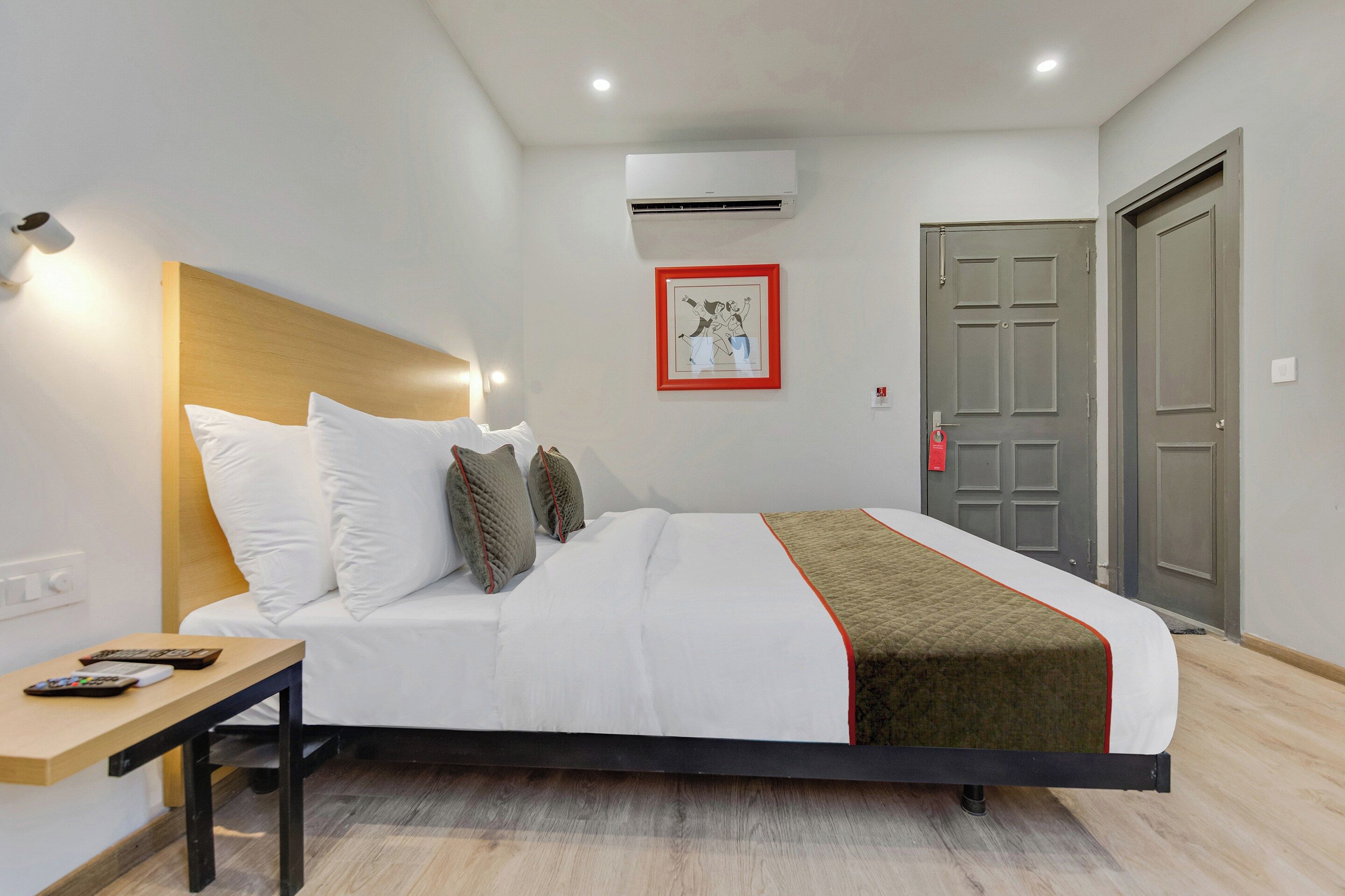 A hotel room with a bed, bedside table, remote control, and a framed picture on the wall.