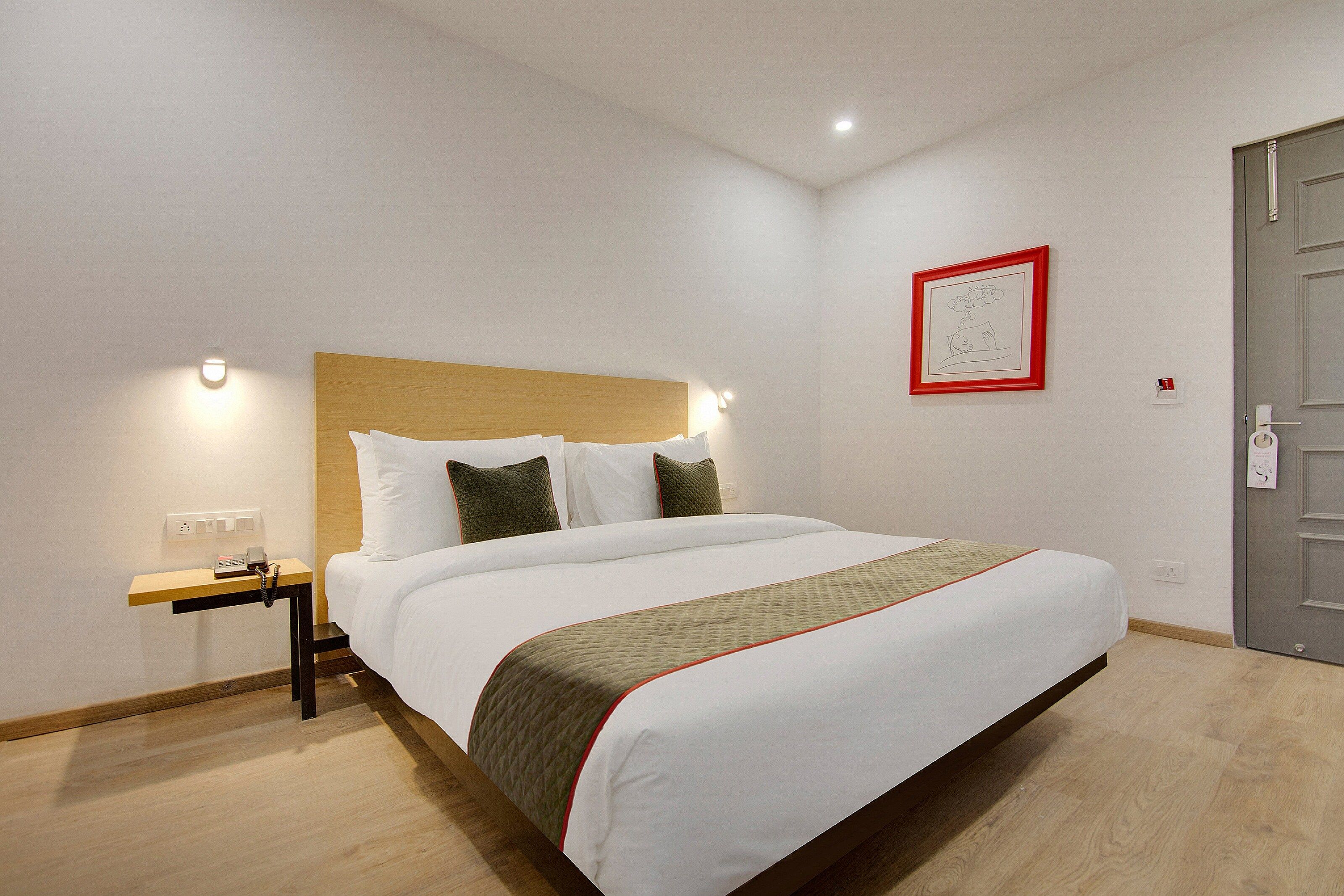 A hotel room with a bed, bedside table, and a framed picture on the wall.